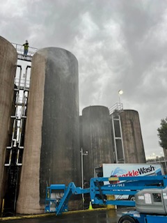 Blue pressure washing equipment positioned in front of large cylindrical storage tanks in Fond du Lac, Wisconsin