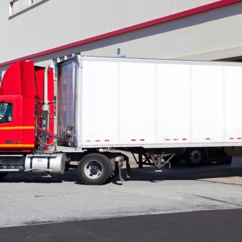 Red semi-truck with white refrigerated trailer parked at loading dock in Fond du Lac, Wisconsin commercial facility