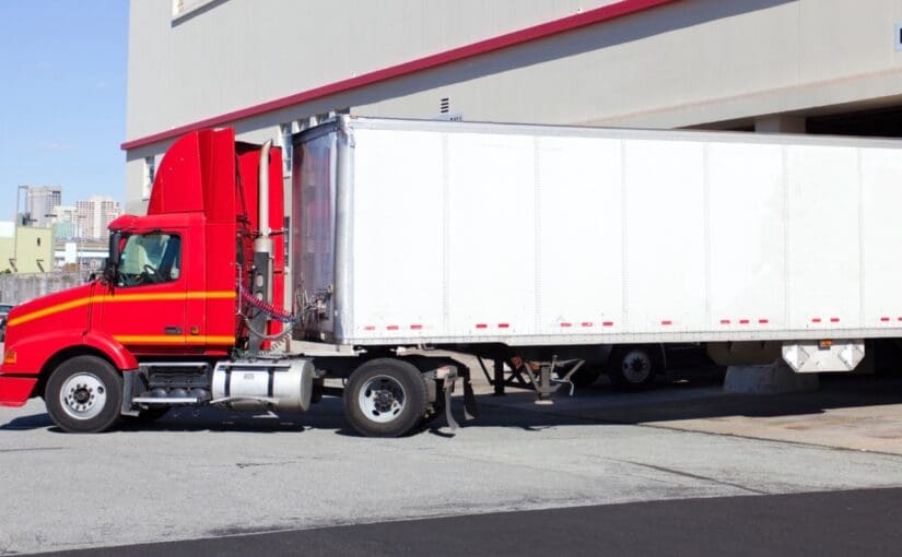 Red semi-truck with white refrigerated trailer parked at loading dock in Fond du Lac, Wisconsin commercial facility