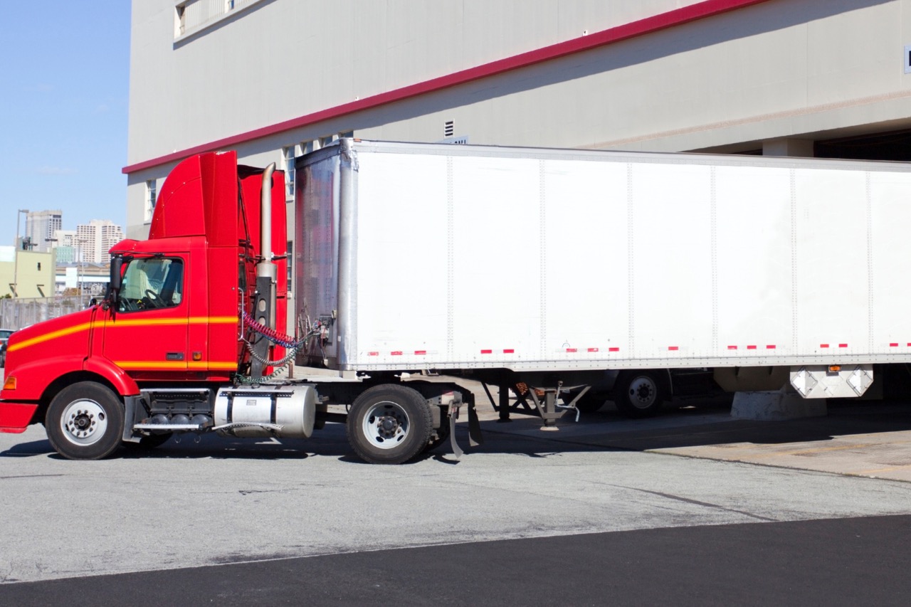 Red semi-truck with white refrigerated trailer parked at loading dock in Fond du Lac, Wisconsin commercial facility