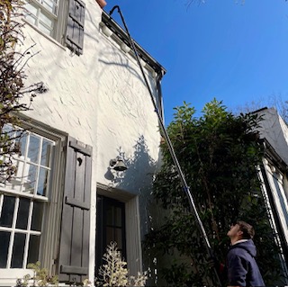 Person using pressure washing equipment to clean gutters and exterior of white residential house in Fond du Lac, Wisconsin under clear blue sky