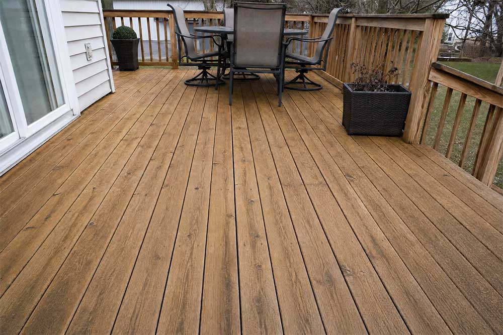 Newly cleaned wooden deck with pressure washing showing restored brown wood grain, paired outdoor seating, and wooden fence railing in Fond du Lac