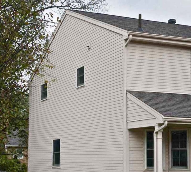 Two-story white vinyl-sided house with dark roof, large front windows, and stone chimney, surrounded by evergreen trees in Fond du Lac, Wisconsin