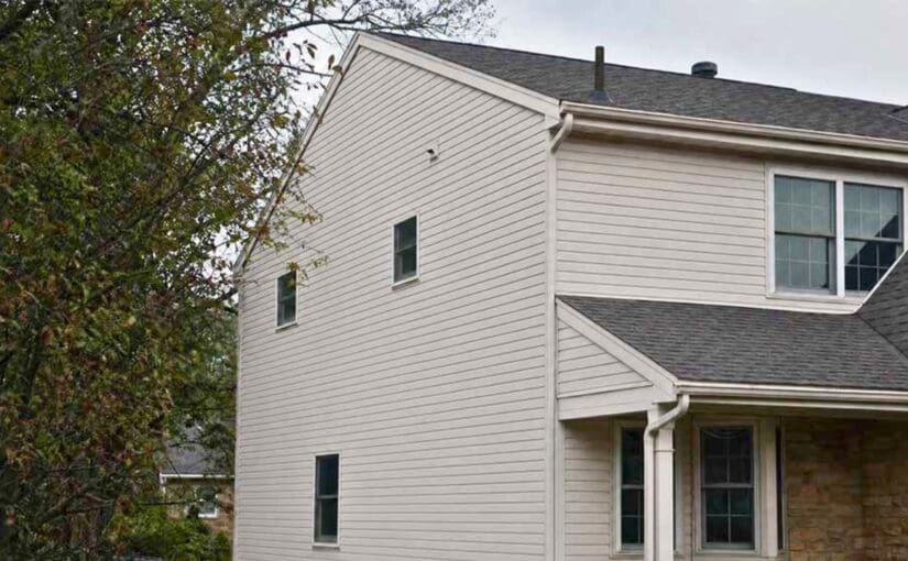 Two-story white vinyl-sided house with dark roof, large front windows, and stone chimney, surrounded by evergreen trees in Fond du Lac, Wisconsin