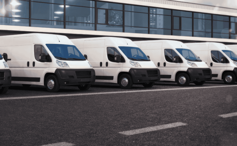 Row of white and blue commercial vans parked in line outside modern building, representing fleet washing and commercial vehicle cleaning services