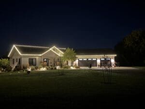Beautifully lit ranch-style home at night in Fond du Lac, Wisconsin, featuring decorative white string lights outlining the roofline, three-car garage, manicured lawn, and landscaping