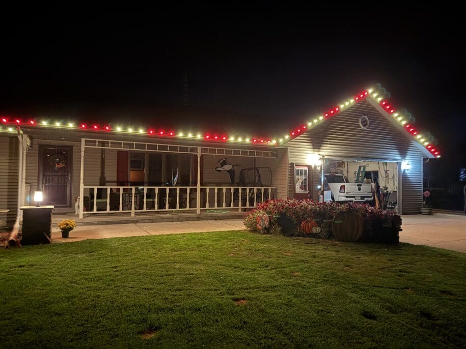 Mobile home at night decorated with red and white holiday lights along the roofline, with fall flower planters and RV in driveway in Fond du Lac, Wisconsin